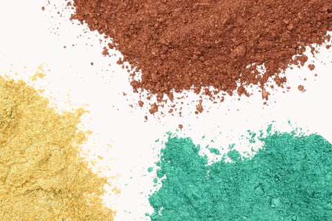 Bowls of colorful mica powder in blue, pink, orange, and gold being used in resin and craft projects.