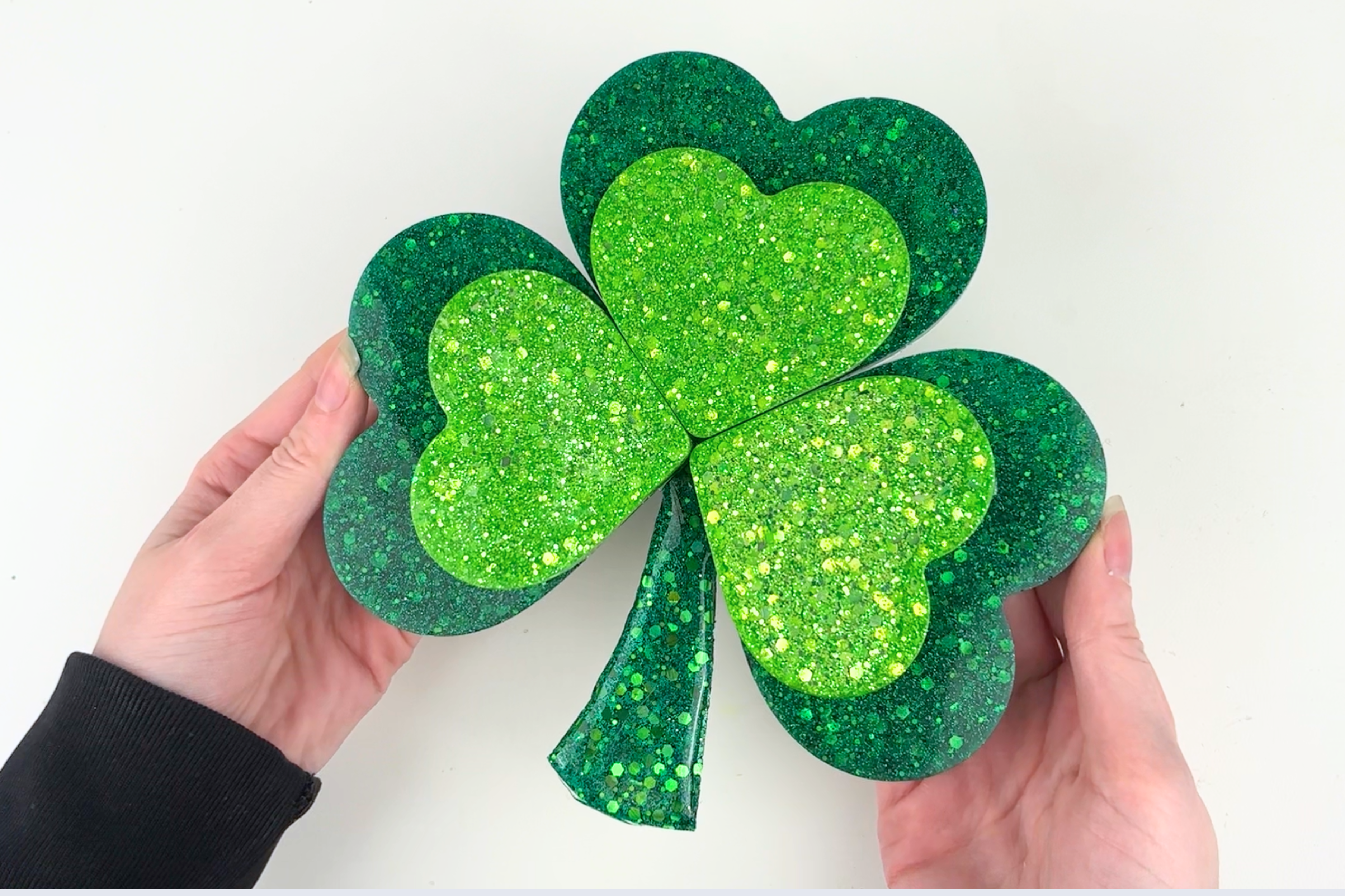 Finished resin shamrock home decor piece with green glitter accents displayed on a shelf for St. Patrick's Day styling.