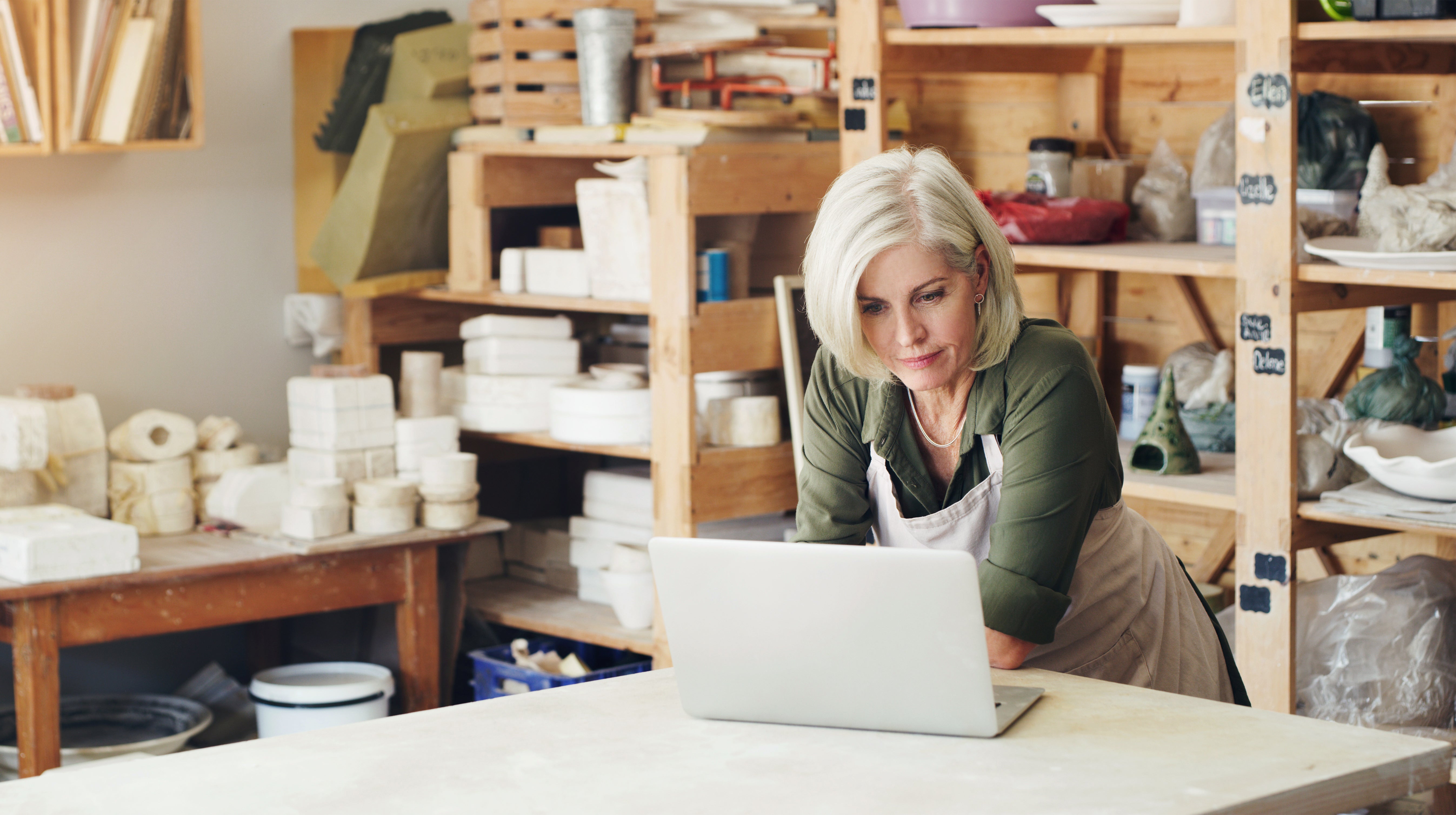 A woman in a pottery studio working on a laptop.