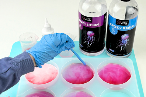 A crafter wearing nitrile gloves and a respirator carefully pouring epoxy resin into a silicone mold in a well-ventilated workspace.