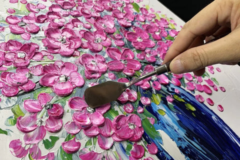 An artist applying super thick acrylic paint to a canvas with a palette knife creating textured peaks and dramatic brush strokes.