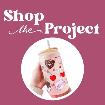 Decorative tumbler with heart and apple designs held by a hand, on a pink background with 'Shop the Project' text.