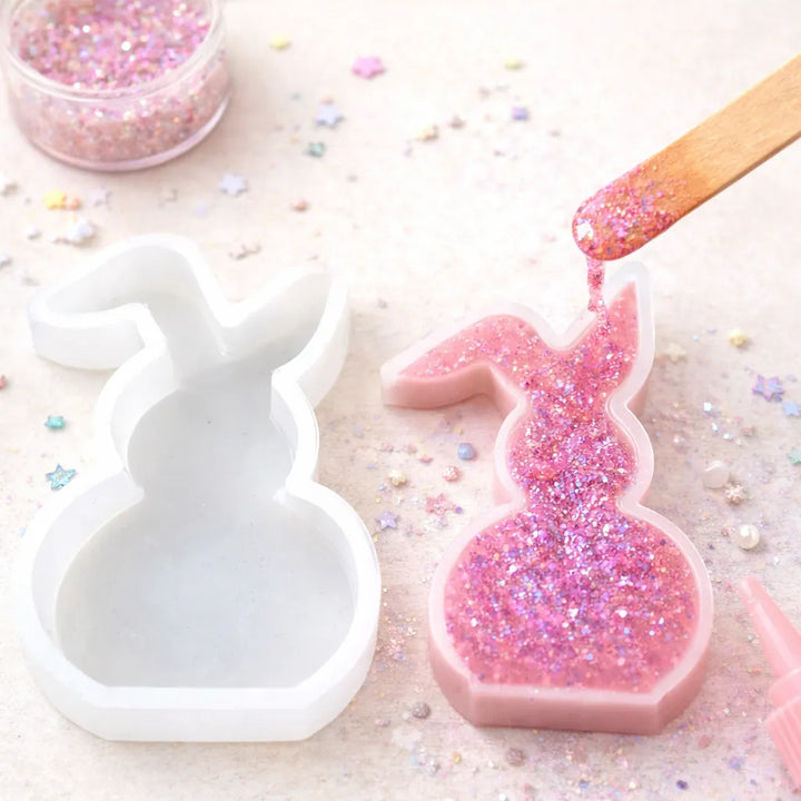 Pink glittery bunny mold being filled with pink glittery substance on a light background.